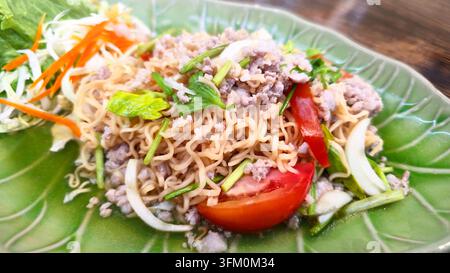 Thai spicy instant noodle salad with minced pork tomato onion celery and fresh vegetables served on a green plate as a popular flavorful Thai dish. Stock Photo