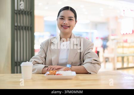 A happy young Southeast Asian Thai businesswoman from the Isan region smiling warmly at the camera. She is wearing a modern beige business blazer, sit Stock Photo