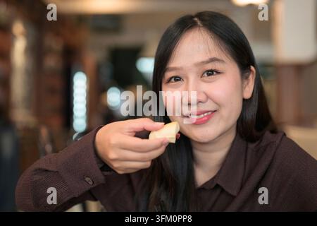 A tight horizontal portrait focusing on a young Asian woman looking directly into the lens with a warm, genuine smile. She is holding a small piece of Stock Photo