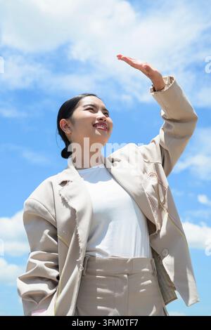 A cheerful vertical portrait of a young Southeast Asian Thai woman from the Isan region standing outdoors and shading her eyes from the bright sunligh Stock Photo