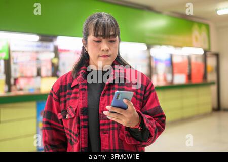 Horizontal medium shot of a person looking down on their phone screen in a bus terminal ticket sales area Stock Photo