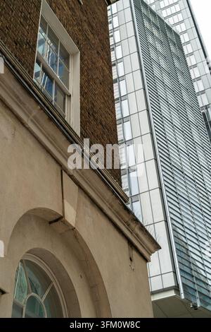 Vertical view of an old stucco and brick building with a sash window, thin metal spikes along the ledge and a round-arched window at the bottom, next Stock Photo