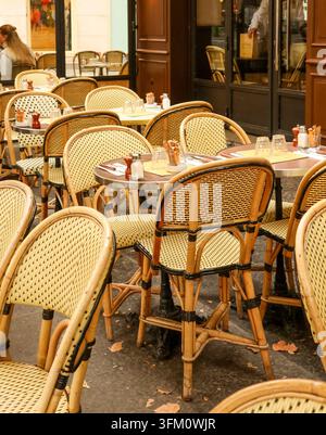 Parisian cafe terrace featuring rows of classic wicker chairs and round tables set for guests, capturing the charming street scene Stock Photo