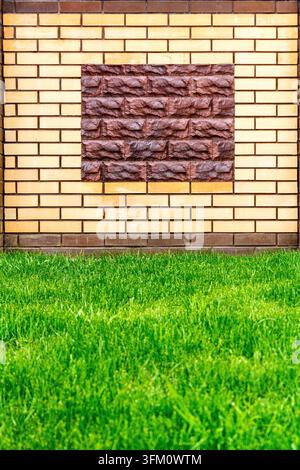 A wall of light brick decorated with a decorative brown stone and green lawn Stock Photo