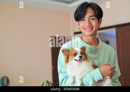 A horizontal lifestyle portrait of a cheerful young Asian man from the Isan region of Thailand standing indoors. He looks directly at the camera with Stock Photo