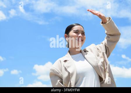 A happy young Southeast Asian Thai woman from the Isan region standing outdoors and shielding her eyes from the sun with her hand. Her dental braces a Stock Photo