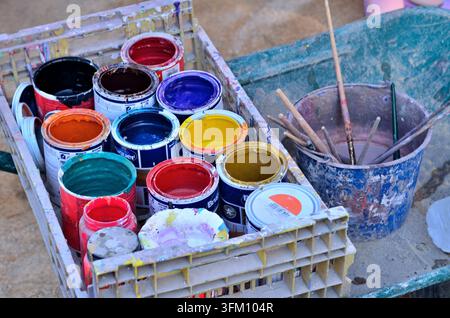 Assorted open paint cans showing various colors with brushes in a bucket Stock Photo
