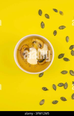 Pea soup with mushrooms in a pink plate stands on a yellow background, pumpkin seeds are scattered around Stock Photo