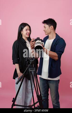 Professional male photographer holding camera and talking with Asian female model beside tripod in photo studio Stock Photo