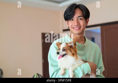A horizontal lifestyle portrait of a cheerful young Asian man from the Isan region of Thailand standing indoors. He looks directly at the camera with Stock Photo