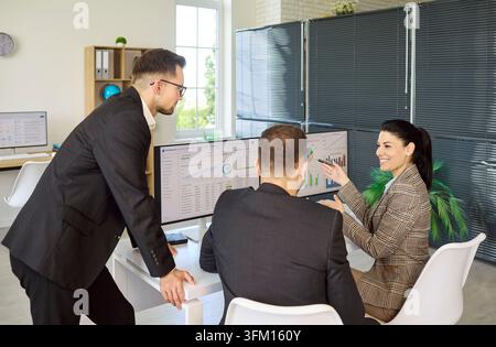 Colleagues review data reports on computer screens during office strategy meeting Stock Photo