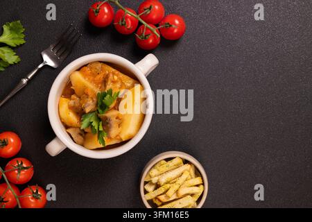 Hearty homemade potato mushroom stone served in a white bowl, garnished with parsley, accompanied by red cherry tomatoes and seasoned beets on a dark Stock Photo