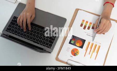 A focused individual analysis of financial data on a laptop while reviewing printed reports. Concept of data-controlled decision making Stock Photo