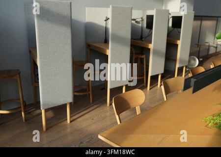 Modern study nook with slim minimalist design. Light wooden tables, padded dividers and cozy chairs. Natural light bathes the quiet workspace. Ideal f Stock Photo