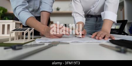 Two people working on a drawing of a house. They use pens and pencils to sketch the design Stock Photo