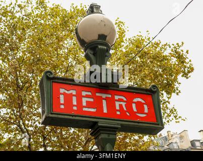 Paris Metro subway sign with classic Art Nouveau design against autumn leaves, symbolizing urban travel and culture in France Stock Photo