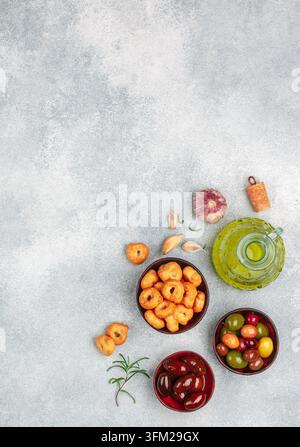 Tarallini-traditional Italian small bagels. Taralli. Tasty snack. Black and green olives, Kalamata, olive oil, garlic and rosemary on a grey concrete Stock Photo