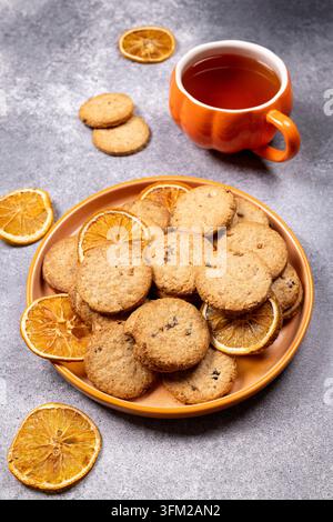 Cookies arranged on an orange platter, decorated with dried orange slices, next to a pumpkin shaped cup filled with hot tea on a gray background, crea Stock Photo