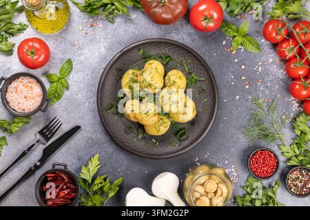 Boiled new potatoes on a dark platter, seasoned with fresh dill and surrounded by various fresh ingredients like tomatoes, herbs, olive oil and spices Stock Photo