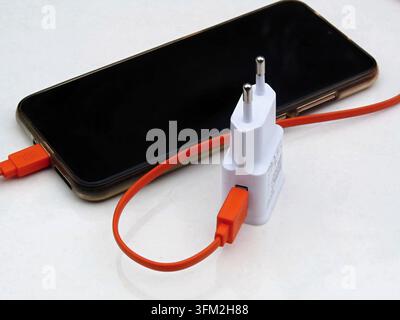Smartphone connected to a white power adapter with a bright orange charging cable Stock Photo