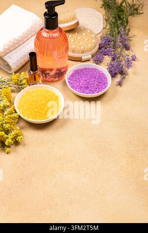 Various spa products, including natural bath salts, essential oil, brushes, lotion dispenser, towels, and fresh lavender and yellow flowers, creating Stock Photo