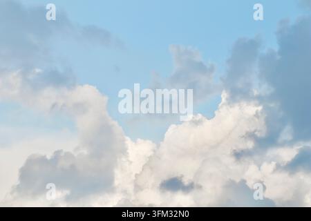 A mix of dark grey storm clouds and bright white cumulus formations against a pale blue sky, showing the transition of weather and dramatic atmospheri Stock Photo