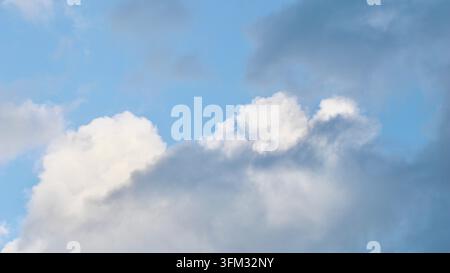 A mix of dark grey storm clouds and bright white cumulus formations against a pale blue sky, showing the transition of weather and dramatic atmospheri Stock Photo