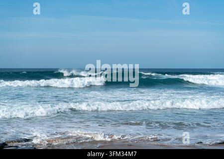 This stunning photograph captures powerful ocean waves crashing onto a sandy beach under a clear, bright sky. The dynamic movement of the water create Stock Photo
