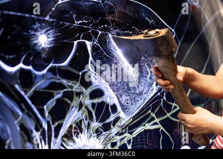 Someone strikes a shattered glass panel using a wooden axe Stock Photo