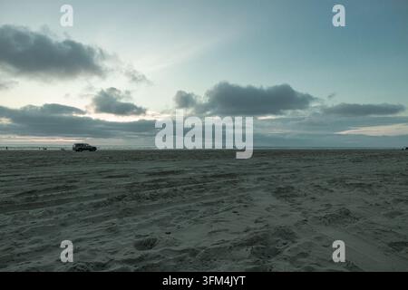 Wide sandy beach at Ocean Shores, Washington at dusk, with tire tracks across the sand, a distant parked SUV and dark clouds over the Pacific horizon. Stock Photo