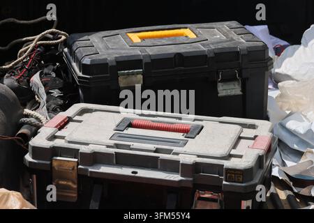 A tool chest with red handle, black toolbox and gray storage case beside rope and equipment in workshop setting Stock Photo