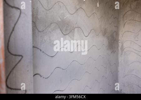A wavy line pattern on weathered concrete wall creating abstract industrial texture with muted gray tones and aged urban character Stock Photo