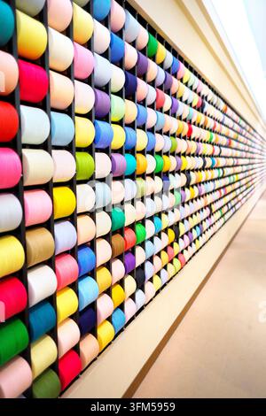August 07, 2023, Imabari, Japan: A large wall display featuring countless spools of colorful thread organized neatly in racks at a textile museum. Stock Photo