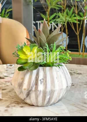 A small decorative arrangement of artificial succulents placed in a white ribbed ceramic pot on a marble surface. Stock Photo