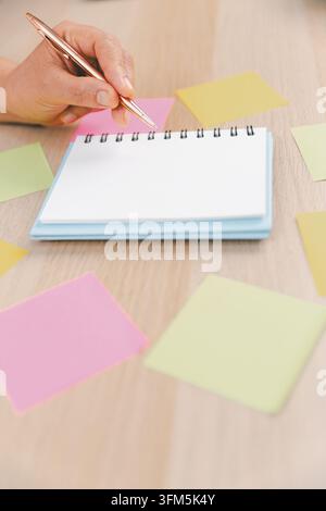 Close-up of a blank spiral notebook with a pen and colorful sticky notes on a wooden desk, representing note taking, planning, reminders, organization Stock Photo