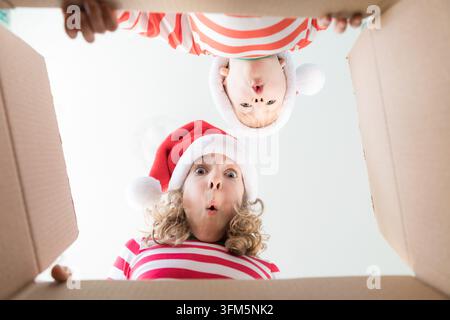 Happy children looking into the box. Funny surprised kids unpack Christmas gift box. Xmas holiday concept. Low angle view. Stock Photo