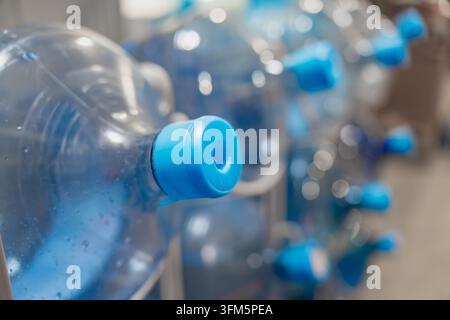 Water cooler bottles with sealed dispensing caps are stored in a rack, illustrating bulk drinking water packaging and container handling for commercia Stock Photo