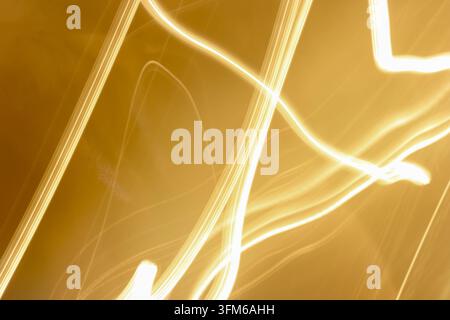 Abstract long exposure photograph featuring sweeping golden and white light trails against a warm amber background. Flowing curves and intersecting li Stock Photo