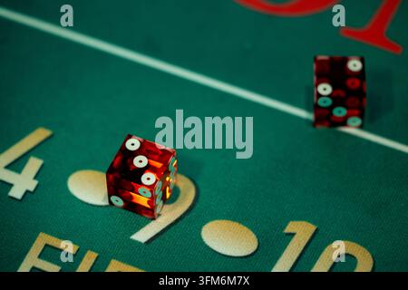 Two red casino dice resting on the green felt layout of a craps table. Close-up shot with sharp foreground focus and soft background blur. Stock Photo