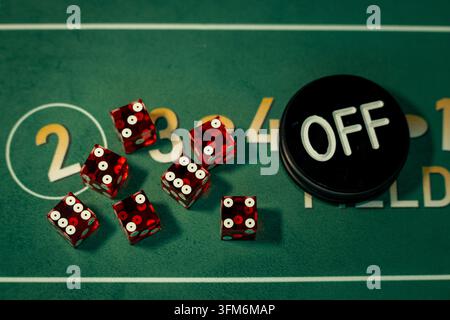 Red dice placed beside a black OFF dealer button on the green felt surface of a craps game table. Visual asset suited for casino night flyers. Stock Photo