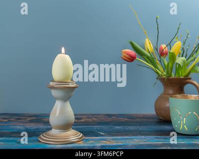 Minimalist Easter still life featuring a white egg shaped candle in an elegant holder on a blue wooden background with spring copy space Stock Photo