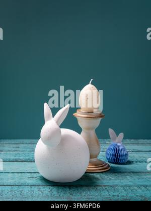 Minimalist Easter still life featuring a white ceramic bunny decorative Easter eggs and small spring ornaments on a turquoise wooden background Stock Photo