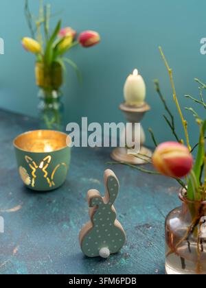 Spring Easter still life with tulips a bunny ornament decorative egg candles and floral decorations on a turquoise blue background Stock Photo