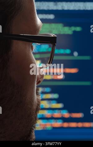 Rear view close up of a programmer in eyeglasses looking at screen with running programming code lines, working on machine learning or artificial intelligence development. Stock Photo