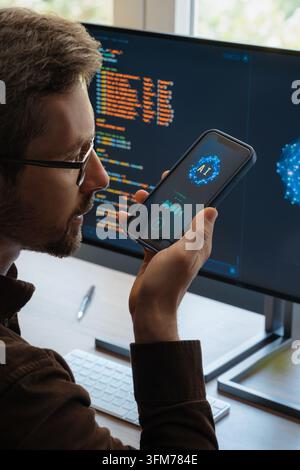 Over-the-shoulder view, of man holding smartphone, talking with AI chatbot app, asking questions, using artificial intelligence assistant for work and daily tasks on phone and computer.  Stock Photo