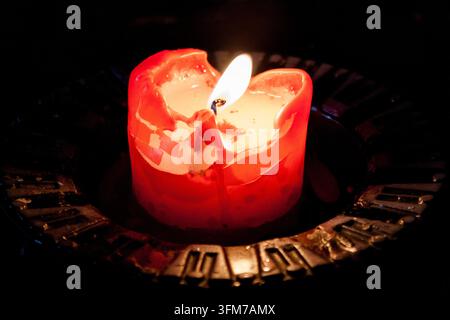 A glowing red candle burns brightly in an ornate metal holder against a dark background in Tallinn, Estonia, its wax melting down the sides Stock Photo