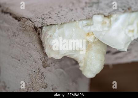 Closeup shows expanding polyurethane foam sealant curing in gap under countertop edge on rough concrete, forming porous yellow white texture for DIY! Stock Photo