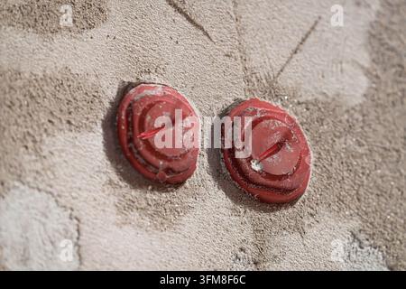 Three red plaster covers on electrical installation boxes embedded in a rough plastered wall showing construction details during interior renovation w Stock Photo