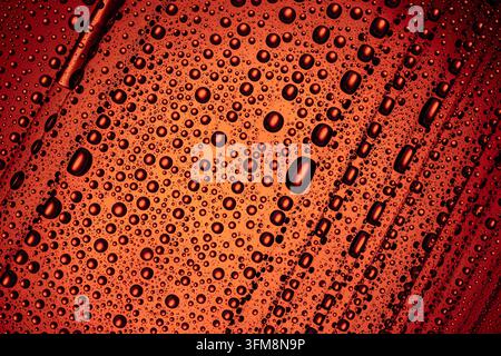 Water drops of various sizes creating an abstract pattern on a textured red surface, showing condensation and moisture Stock Photo