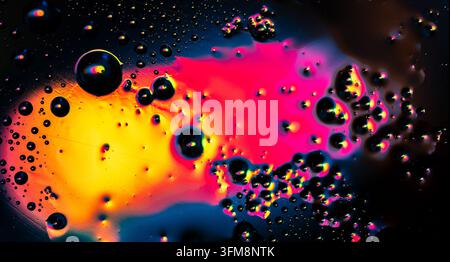 Macro view of oil and water drops mixing with vivid pink, yellow, orange, and blue colors on a dark background Stock Photo